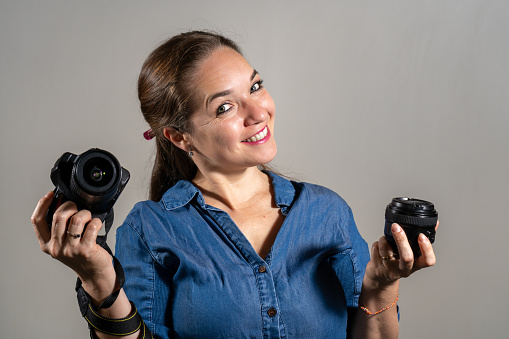 Young woman comparing a professional camera with a new lens.  Young woman deciding between buying a new camera or a new lens. Woman with a camera and lens in her hands.