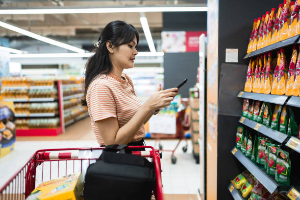 istock woman Looking At Smartphone While Choosing Items In Supermarket 2114595679