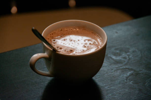 A white cup of fresh black coffee on a saucer, served with a single chocolate on a rustic burlap background
