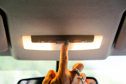Woman's hand turning on a car interior light.