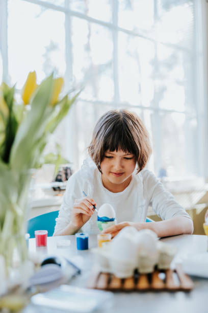istock A young child sits at the kitchen table, completely absorbed in the delightful task of painting Easter eggs 2114627678
