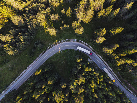 Drone point of view over two semi-trucks on a road curve in pine woodland.