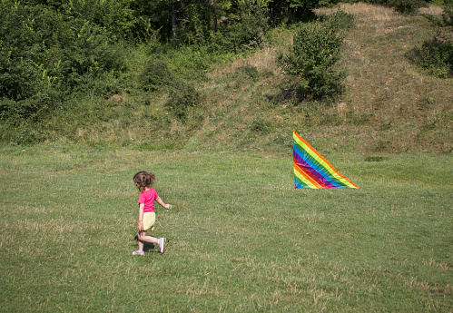 Happy child girl running with kite in the green field in Spring outdoor