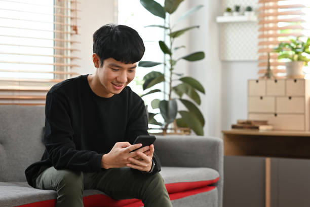 istock Portrait with Millennial Young Asian male using smartphone while sitting on sofa. 2114721276