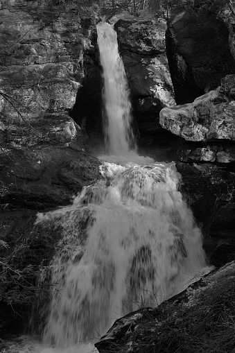 Kent Falls in Connecticut. Long view of upper falls after rain, early spring. Widely considered the most spectacular waterfall in the state and one of the best in New England. In rural Litchfield County, Kent Falls is a popular state park. You park near the bottom of the half-mile trail and follow it to the top, with viewing platforms along the way. The falls are 250 feet high. Black-and-white photo.