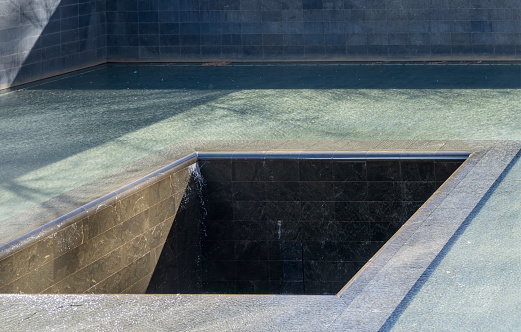 Manhattan, New York, USA - March, 2024.  World Trade Centre memorial ground zero waterfall feature.
The National September 11 Memorial & Museum (also known as the 9/11 Memorial & Museum) is part of the World Trade Center complex, in New York City, created for remembering the September 11 attacks of 2001. The memorial is located at the World Trade Center site, the former location of the Twin Towers that were destroyed during the September 11 attacks. The designer of the Memorial is Israeli-American architect Michael Arad of Handel Architects. Arad worked with landscape-architecture firm Peter Walker and Partners on the design to create two square reflecting pools in the center marking where the Twin Towers stood. A dedication ceremony commemorating the tenth anniversary of the attacks was held at the memorial on September 11, 2011, and it opened to the public the following day. The museum was dedicated on May 15, 2014 Six days later, the museum opened to the public.