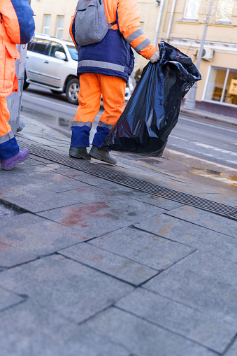 A worker in special clothes carries a black bag with garbage