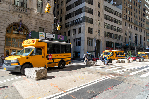 Wall Street, Manhattan, New York, USA - March, 2024.  New York yellow school buses near the Wall Street Bull statue.