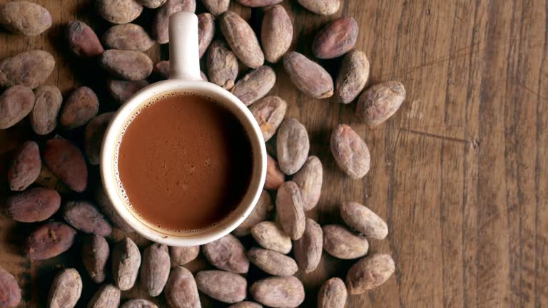 Top view of hot chocolate drink, cocoa drink and natural cocoa powder with brown cocoa beans and dry cacao pod  on a vintage wooden table.