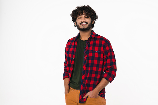 Happy Indian young man in casual clothes looking at camera isolated over white background. Cheerful Hindi boy with curly hair and beard in relaxed posture pose