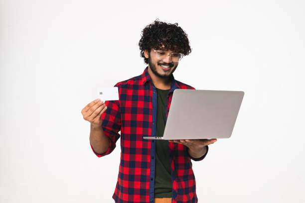 istock Cheerful Indian young man using laptop for e-banking with credit card isolated 2114837672