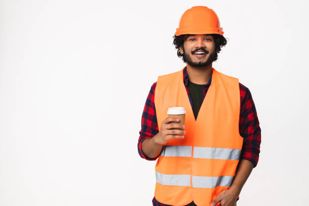 istock Happy young Indian construction worker in orange uniform and helmet drinking coffee isolated 2114840309
