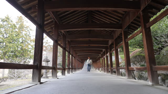 Japanese tourist walking on long corridor of shrine in the morning - part 1 of 3