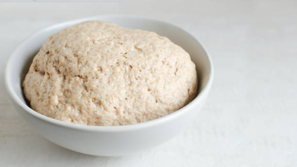 Dough from whole wheat flour in a gray bowl on a gray background. The process of making bread at home. Concept of healthy food. Horizontal orientation. Copy space. Selective focus. stock photo