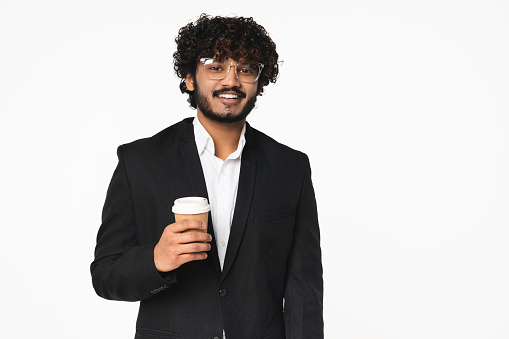Young Indian businessman in formal black suit drinking coffee isolated over white background. Cheerful Hindu manager CEO boss with hot beverage in eco-friendly recycling cup