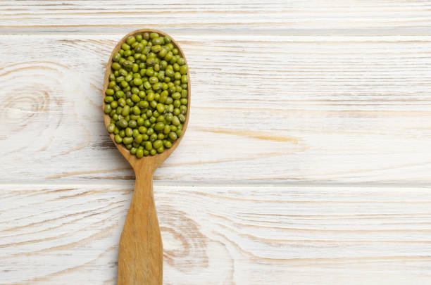 Green mung beans in a large spoon on a white wooden background. Organic legumes. Vegan and vegetarian food. The concept of healthy eating. Horizontal orientation. Copy space. Top view. stock photo