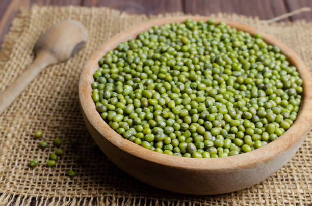 Green mung beans in a bowl on burlap on a wooden table. Organic legumes. Vegan and vegetarian food. Rustic style. The concept of healthy eating. Horizontal orientation. Selective focus. stock photo