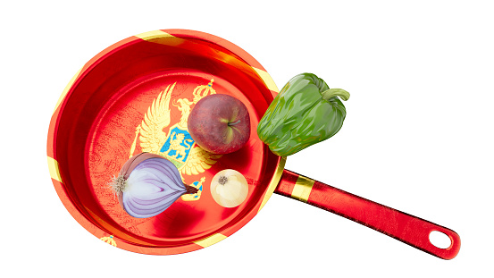 A dynamic composition featuring a red pan decorated with the Montenegrin coat of arms, surrounded by vibrant, fresh vegetables.