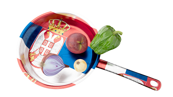 A culinary image featuring a frying pan with a representation of the Serbian coat of arms, accompanied by ripe vegetables.