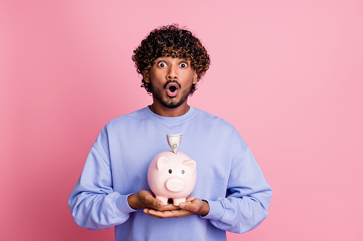 Photo of surprised impressed guy wear stylish blue clothes hold piggy bank deposit financial future isolated on pink color background.