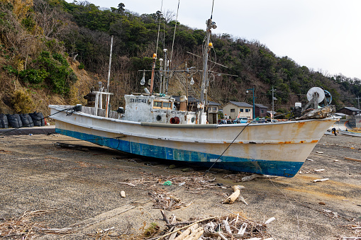 Scenic view of white fishing boat on beach of the Pacific Ocean at Japanese seashore with woodland in the background. Photo taken February 14th, 2024, Japan.