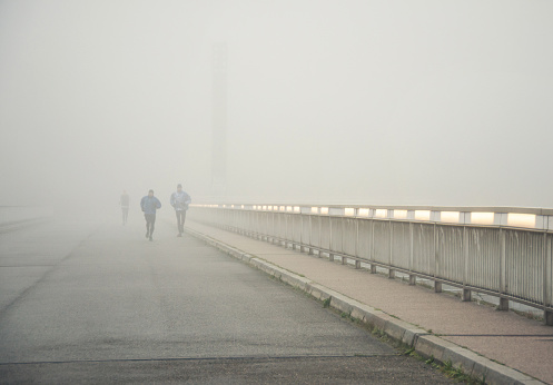 Vienna, Austria - November 17, 2013: Few joggers running along the bridge in low visibility. Early autumn morning.