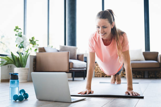 istock Strong Caucasian woman standing in plank position while watching online video training on laptop 2114966797