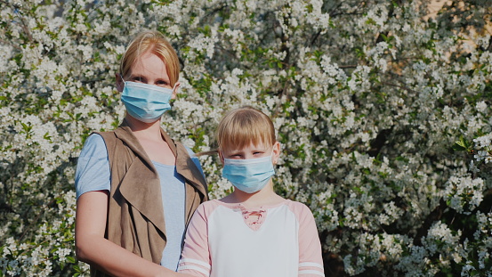 Woman with children in gauze bandages against the background of flowering trees. Allergy problems in the spring.
