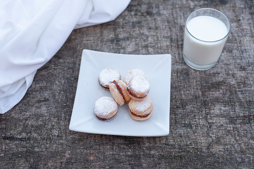 Freshly baked cookies on plate with glass of milk on wooden table.