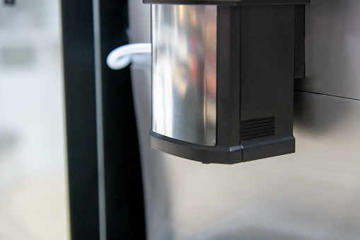 Close-up view of metal combi spout with coffee, milk and powder drink outlets of modern automatic table top bean-to-cup coffee vending machine. Soft focus. Hot drinks equipment theme.