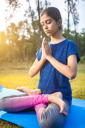 portrait of a young girl practicing padmasana and Pranamasana yoga in the park