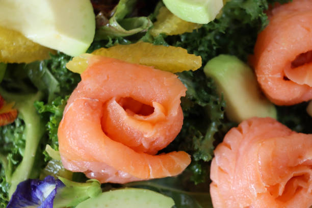 Stock photo showing close-up, elevated view of healthy smoked salmon, avocado and grapefruit salad with mixed lettuce leaves and a garnish of edible flower petals.