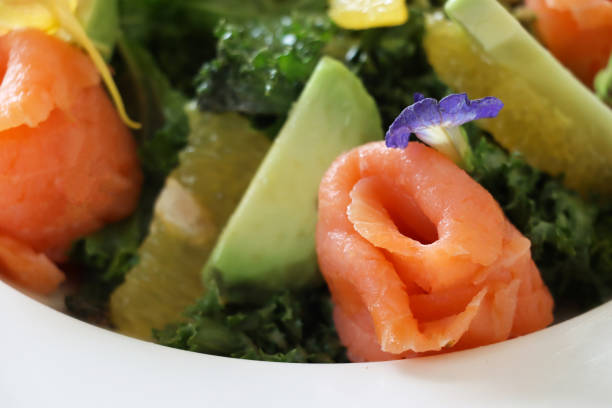 Stock photo showing close-up, elevated view of healthy smoked salmon, avocado and grapefruit salad with mixed lettuce leaves and a garnish of edible flower petals.
