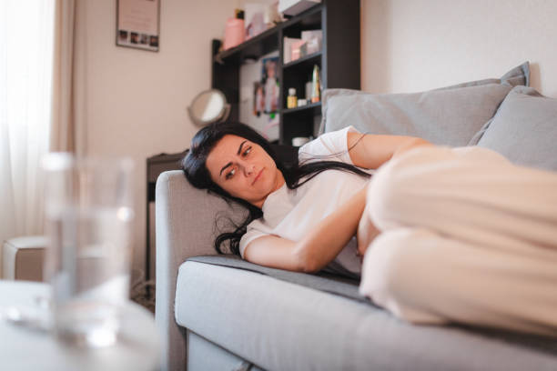istock Young woman lying down while holding her stomach in pain 2115075519