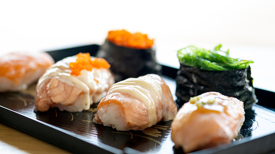 An exquisite selection of sushi pieces, featuring creamy toppings and fresh garnishes, presented on a sleek black serving tray