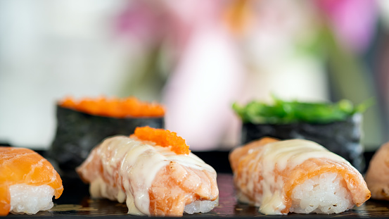 A sushi set highlighted by the creamy toppings and tobiko, elegantly arranged on a black tray, with a soft-focus background enhancing the vibrant colors
