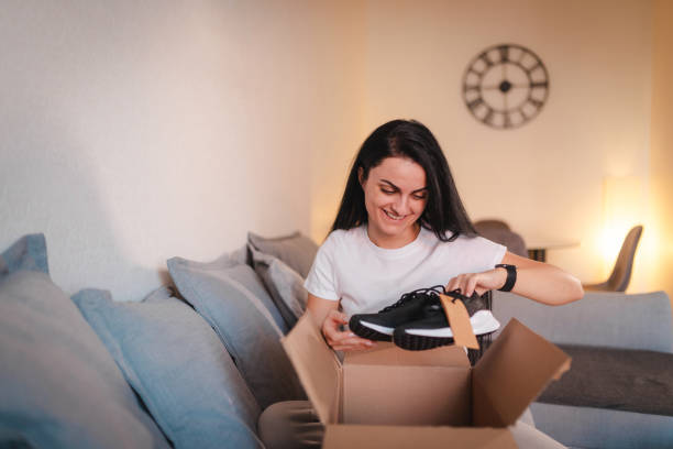 istock Happy young woman opening a package containing shoes she ordered online 2115090544