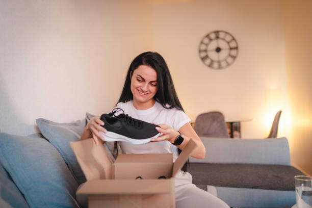 istock Happy young woman opening a package containing shoes she ordered online 2115090547