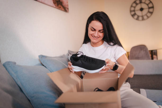 istock Happy young woman opening a package containing shoes she ordered online 2115090561