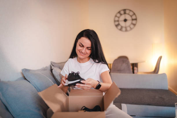 istock Happy young woman opening a package containing shoes she ordered online 2115090564