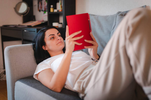 istock Beautiful young woman lying on her back and reading a book 2115098072
