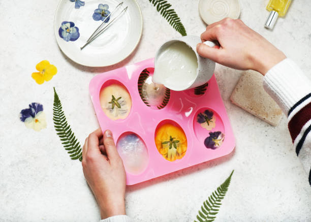 istock Step. 3 Pouring liquid homemade soap mass into silicone mold. The process of making handmade organic soap with pressed flowers, fern leaves. 2115101770