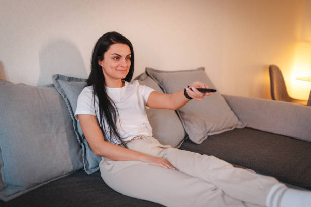 istock Young woman relaxing on the sofa at home while watching television 2115101779