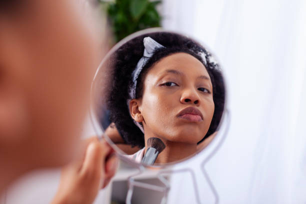 istock black girl putting on makeup at home holding a small mirror 2115104974