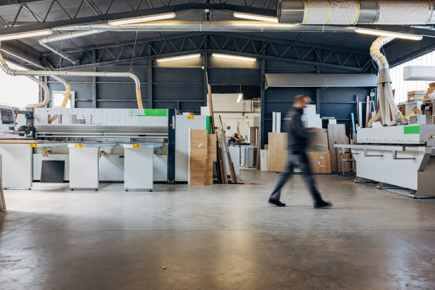 istock Interior of a workshop with a craftsman transporting wood to a processing machine 2115119235