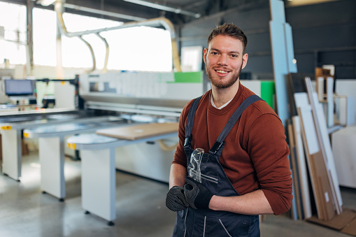 Portrait of a handsome man standing with crossed arms in a workshop and looking directly at the camera