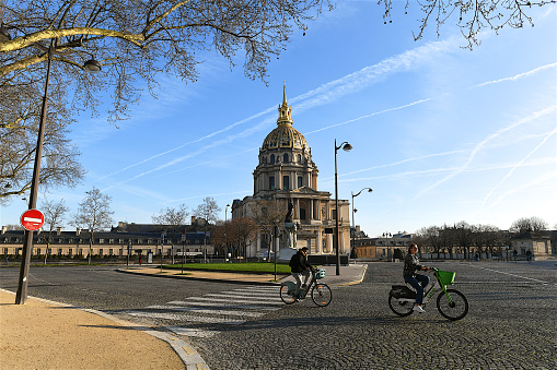 Paris, France-03 21 2024: Two people passing in front of the Invalides, formally the National Residence of the Invalids, is a complex of buildings containing museums and monuments, all relating to the military history of France, as well as a hospital and a retirement home for war veterans, the building's original purpose, Paris, France.