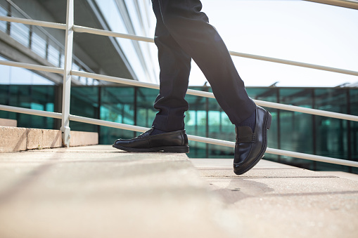 Cropped shot of male legs as unrecognizable businessman walking upstairs, taking confident steps on city stairs, symbolizing career opportunities and growth, in urban area outside