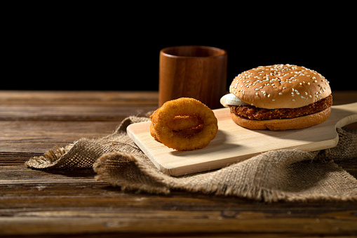 Rustic burger and crispy onion rings, wooden cutting board, burlap texture, warm lighting
