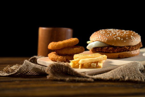 Gourmet Burger setup with onion rings and sides, wooden texture, rustic vibe, highlighted by warm light